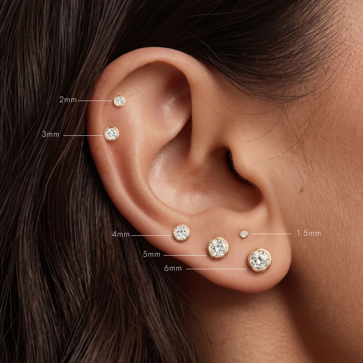 14K Yellow Gold Bezel Studs in sizes 1.5mm to 6mm worn on the ear with size labels